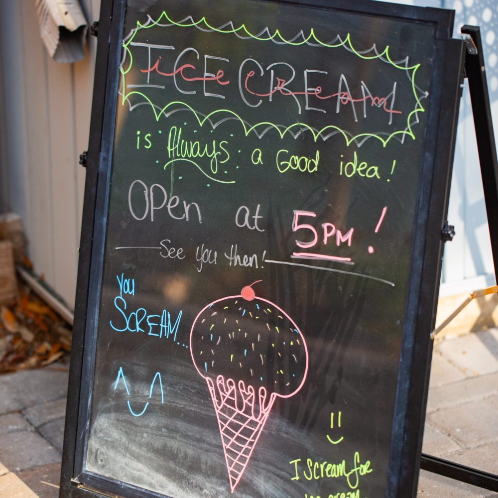 A sidewalk chalkboard sign announces ice cream, noting it is always a good idea and opens at 5 p.m., with colorful drawings of an ice cream cone and playful text.