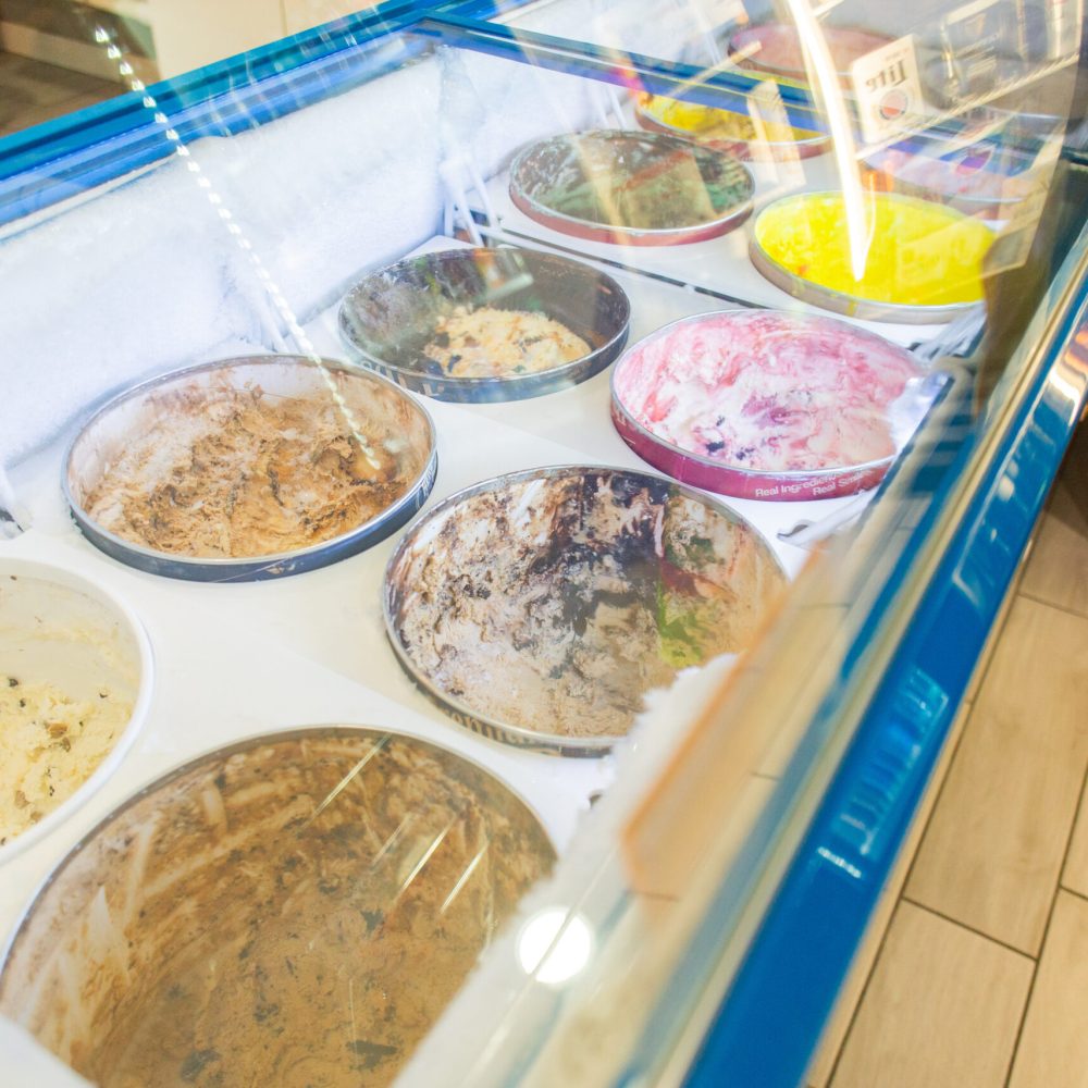 An ice cream display freezer with several partially empty tubs of various ice cream flavors, seen from above.